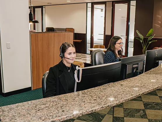 Two Servcorp receptionists wearing headsets are professionally managing calls and client inquiries at a polished front desk